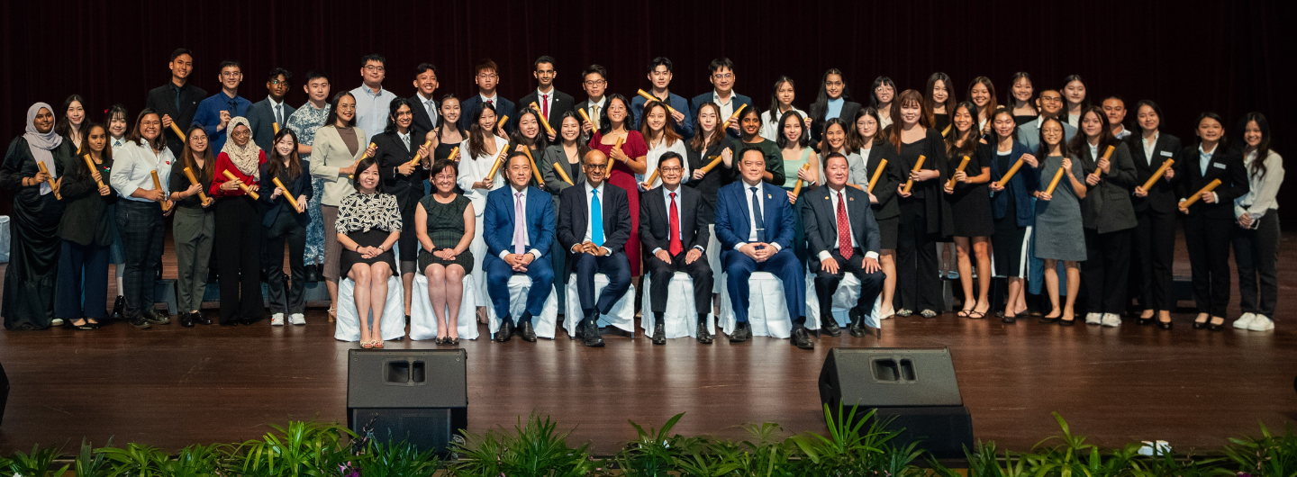 Large group of people holding diplomas, seated and standing on a stage.